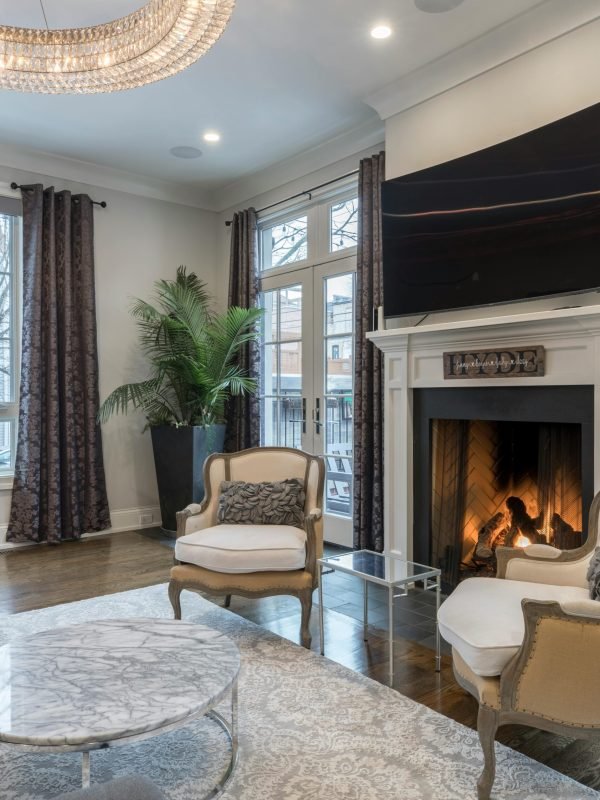 Upscale living room interior featuring fireplace, crystal chandelier, hardwood floors, and classic armchairs